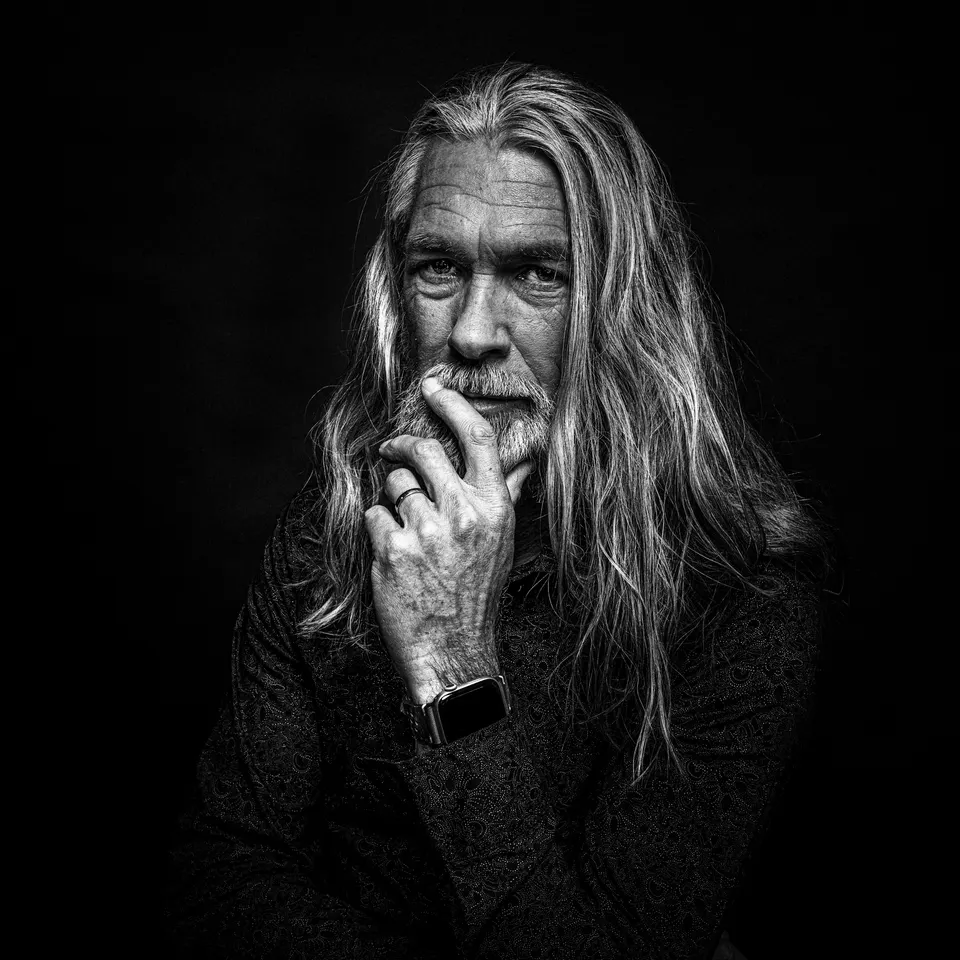 Portrait eines Mannes mit langem grauem Haar, die Hand am Kinn, schwarzweiß