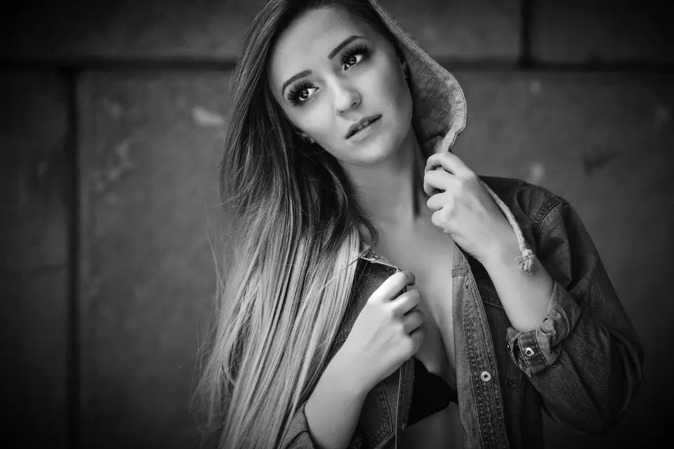 Frau mit langem Haar und Jeansjacke vor Betonwand, schwarzweiß